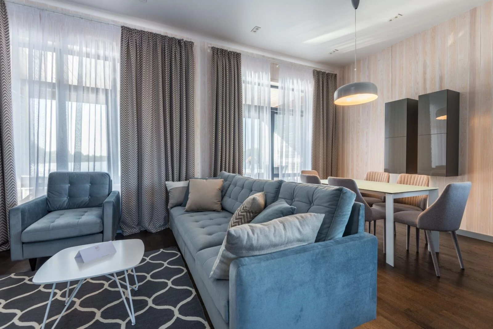 Salon meublé et lumineux, avec canapé, fauteuil et table près des fenêtres